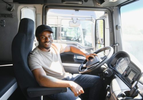 Professional african american truck driver in casual clothes driving truck vehicle going for a long transportation route.